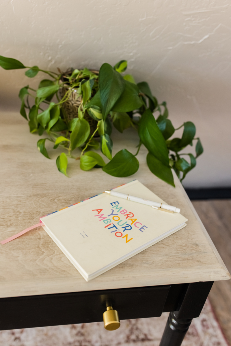 a notebook flatlay with "embrace your ambition" on the front and a pen on top of it