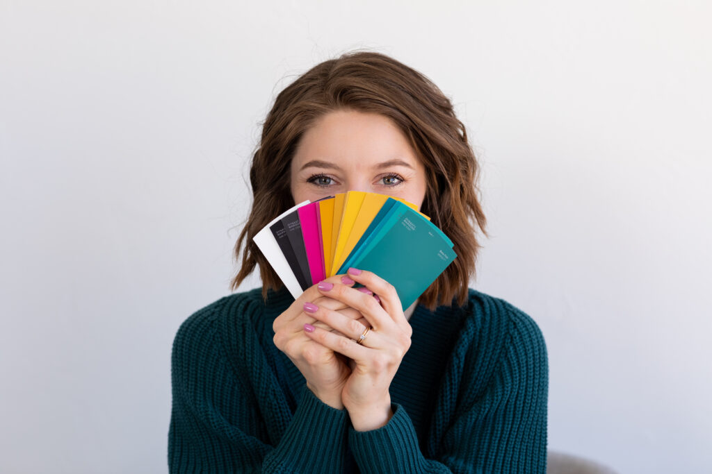 a woman holding up colorful swatches in front of her face